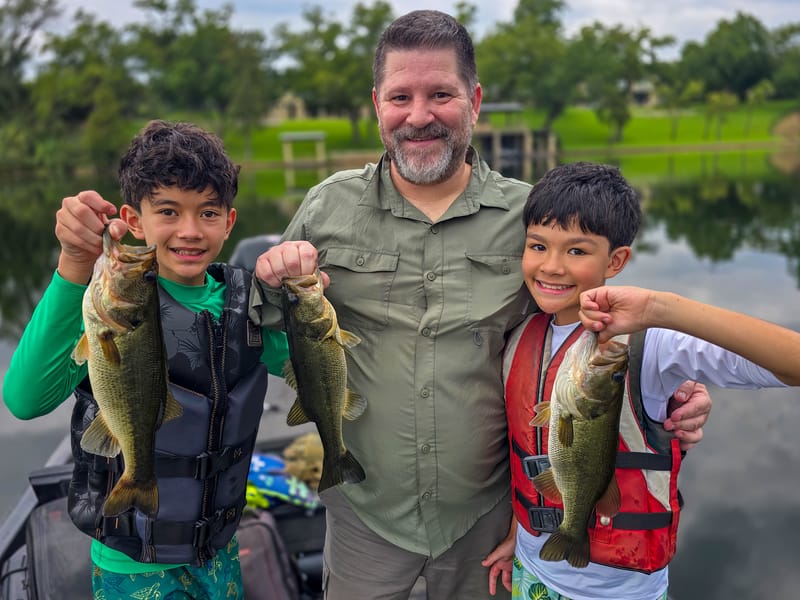 Father and two boys each holding largemouth bass on a Lake Austin guided fishing trip